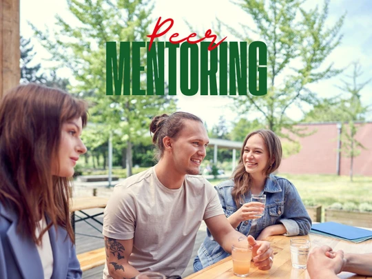 Napis "Peer-mentoring" a w tle grupa studentów siedząca przy stołówce